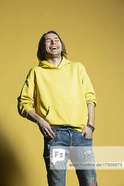 Glücklicher Mann in Jeans und Kapuzenpulli lachend gegen gelben Hintergrund