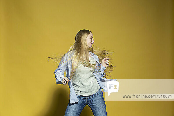 Unbeschwerte junge Frau tanzen gegen gelben Hintergrund