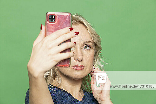 Schöne blonde Frau nimmt Selfie auf grünem Hintergrund