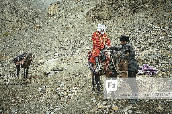 Ein Mann hilft seiner schwangeren Frau auf ein Pferd  kirgisische Nomaden  Wakhan-Korridor  Badachschan  Afghanistan  Asien