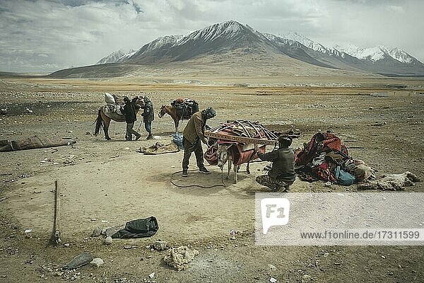 Two men load a donkey with components of a yurt in front of moving to winter camps  Bozai Gumbaz  Wakhan Corridor  Badakhshan  Afghanistan  Asia