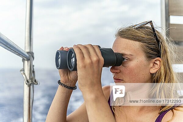 Junge Frau schaut durch ein Fernglas  auf Segelboot  Dodekanes  Griechenland  Europa