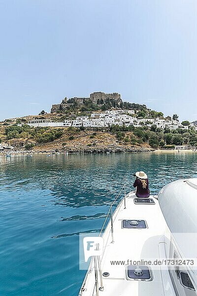 Junge Frau sitzt auf Segelboot und schaut auf das türkise Meer  hinten Akropolis von Lindos  antiken Zitadelle auf einer steilen Klippe  Lindos  Rhodos  Dodekanes  Griechenland  Europa