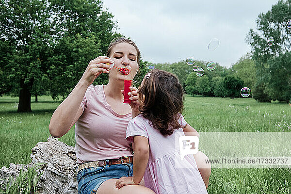 Verspielte Mutter  die mit ihrer Tochter im Park Seifenblasen bläst