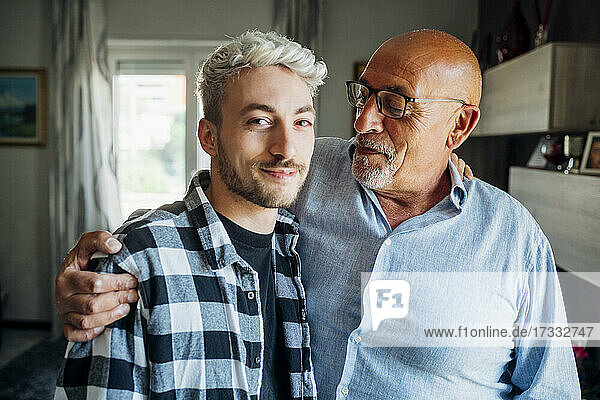 Father with arm around looking at son while standing at home