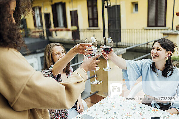 Freundinnen stoßen auf der Terrasse sitzend mit Weingläsern an