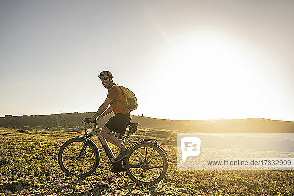 Mature sportsman with backpack riding electric bicycle at sunset
