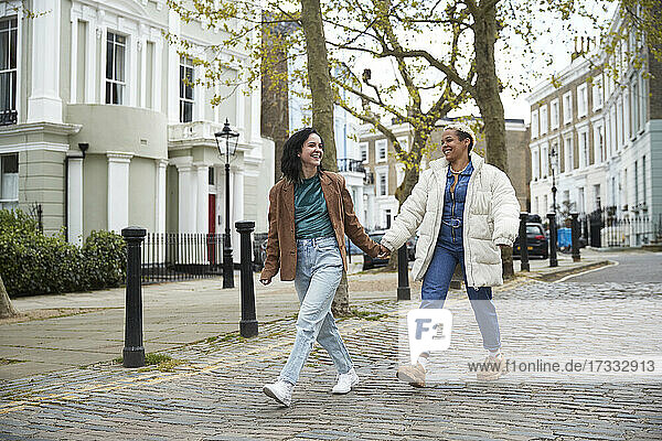 Glückliches lesbisches Paar  das sich die Hände hält  während es gemeinsam auf dem Fußweg geht