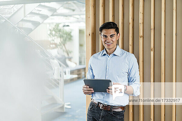 Lächelnder Geschäftsmann mit digitalem Tablet im Büro stehend
