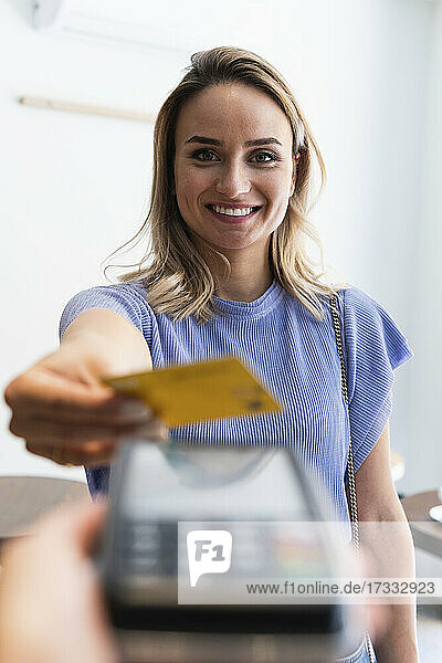Lächelnde junge Frau beim Bezahlen mit Kreditkarte in einem Café