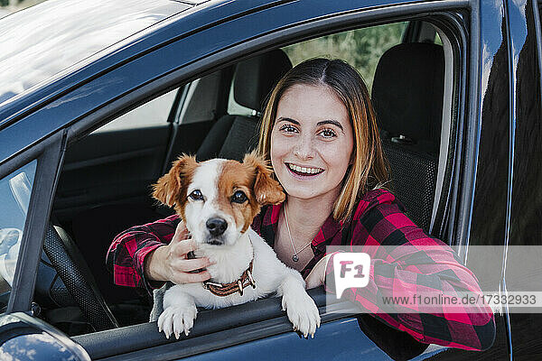 Beautiful happy young woman with dog sitting in car