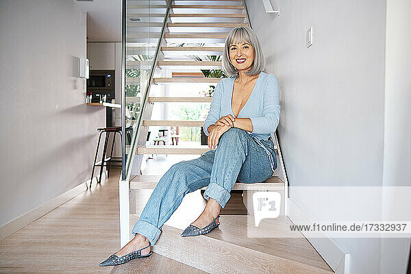 Smiling mature woman sitting on staircase at home