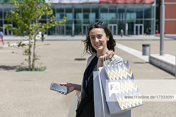Smiling woman with smart phone holding shopping bags
