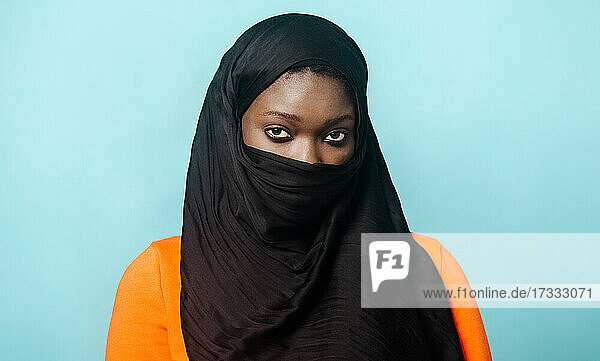 Young woman wearing hijab standing against blue background