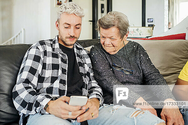 Junger Mann teilt Mobiltelefon mit Großmutter zu Hause