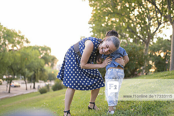 Fröhliche Großmutter spielt mit ihrem Enkel auf einer Wiese in einem öffentlichen Park