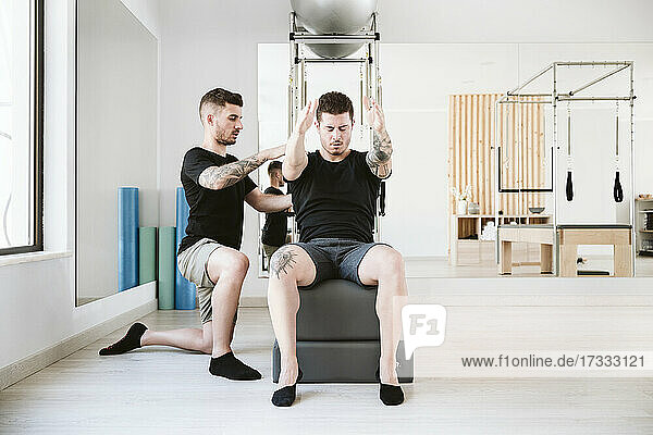 Männlicher Fitnesstrainer  der einem Mann bei der Ausübung von Pilates im Studio hilft