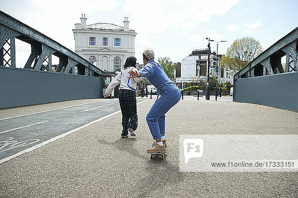Woman skateboarding while enjoying with girlfriend on bridge