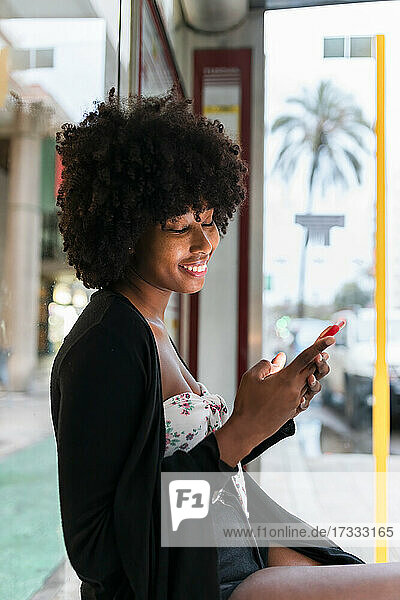 Smiling Afro woman using smart phone at bus top