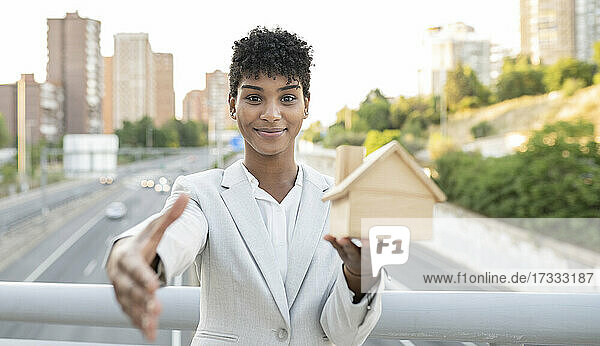 Verkäuferin  die ein Hausmodell hält  während sie auf einer Brücke mit Handschlag begrüßt
