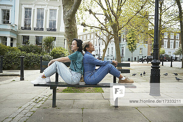 Weibliches lesbisches Paar sitzt Rücken an Rücken auf einer Bank in der Stadt