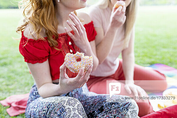 Frau hält Donut  während sie mit einem Freund im Park sitzt