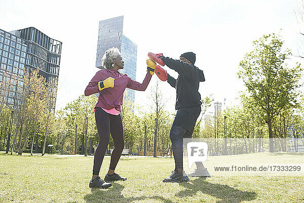 Senior woman practicing boxing with man at park on sunny day