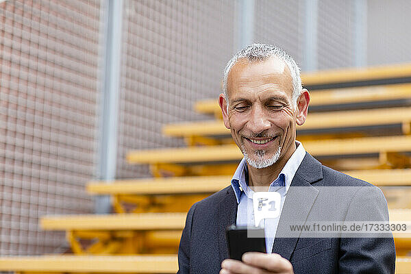 Lächelnder männlicher Fachmann  der ein Smartphone auf einer Treppe benutzt