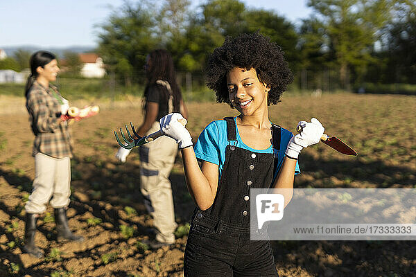 Lächelndes Mädchen mit Kelle und Harke auf einem Bio-Bauernhof an einem sonnigen Tag