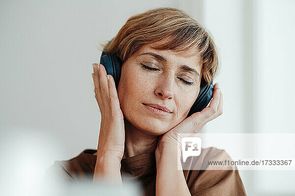 Weibliche Fachkraft mit geschlossenen Augen hört Musik über Kopfhörer im Büro