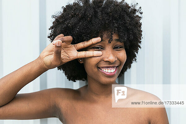 Smiling Afro woman gesturing in front of wall