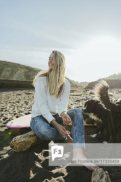 Lächelnde blonde Frau schaut weg  während sie mit ihrem Hund am Strand sitzt
