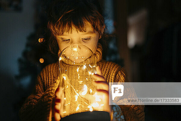 Girl looking at Christmas decoration lights in dark at home