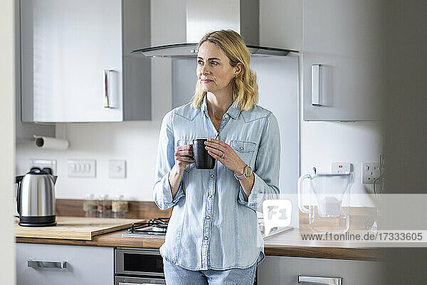 Frau mit Teetasse  die wegschaut  während sie in der Küche zu Hause steht