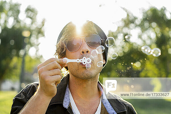 Young man wearing sunglasses blowing bubbles at park
