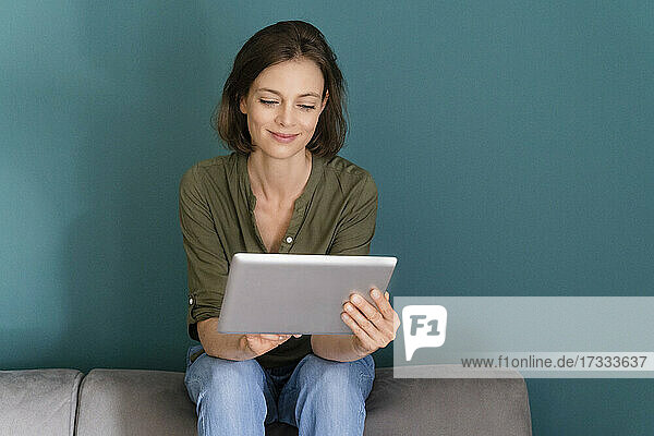 Lächelnde Frau  die ein digitales Tablet benutzt  während sie auf dem Sofa sitzt