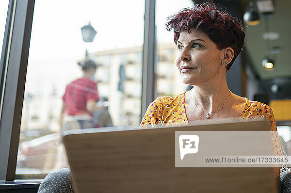 Ältere Frau mit Laptop schaut durch das Fenster eines Cafés