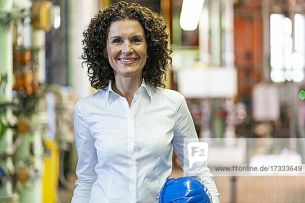Smiling female expert with hardhat standing at industry