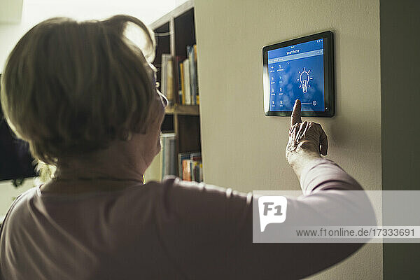 Senior woman using futuristic smart home device on wall