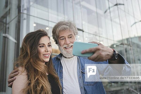 Glücklicher Vater nimmt Selfie mit Tochter durch Smartphone vor Glasgebäude