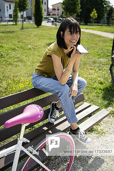 Woman sending voice message through smart phone while sitting on bench