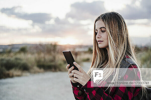Junge schöne Frau mit blonden Haaren Textnachrichten über Smartphone bei Sonnenuntergang
