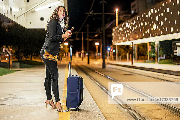 Businesswoman with mobile phone waiting on tram station at night