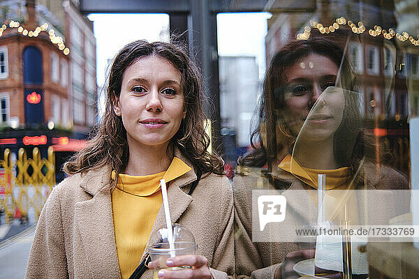 Frau mit Saftglas lehnt an Schaufenster eines Geschäfts