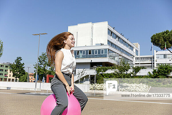 Lächelnde weibliche Freiberuflerin genießt auf Hüpfball auf der Straße während sonnigen Tag