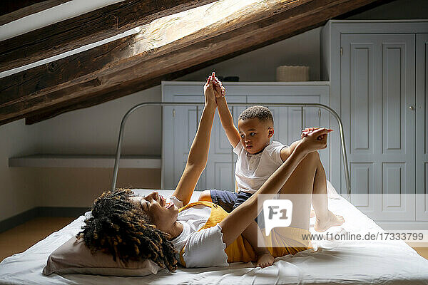 Happy mother playing with son while lying on bed in attic at home