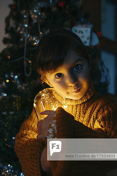 Cute girl in sweater holding Christmas lights at home