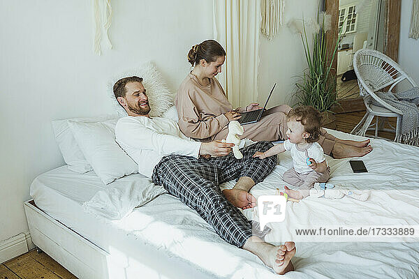 Mann spielt mit Tochter von Frau mit Laptop auf Bett zu Hause