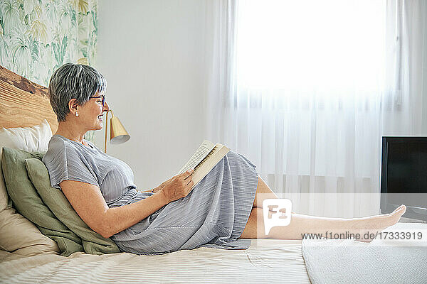 Frau liest ein Buch und entspannt sich auf dem Bett zu Hause