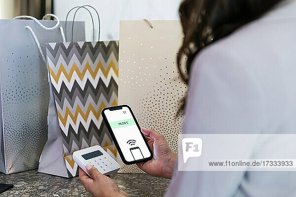 Frau hält Smartphone  während sie in einer Boutique kontaktlos bezahlt